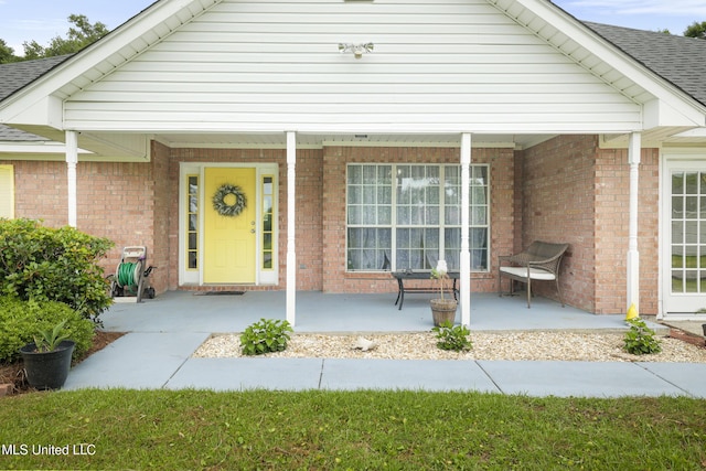 doorway to property with a porch, brick siding, and a shingled roof