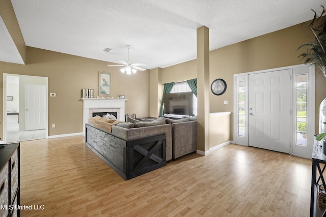 living room with light wood-type flooring, a ceiling fan, baseboards, and a fireplace