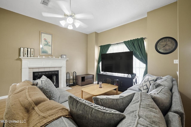 living area with ceiling fan, wood finished floors, a tiled fireplace, and baseboards