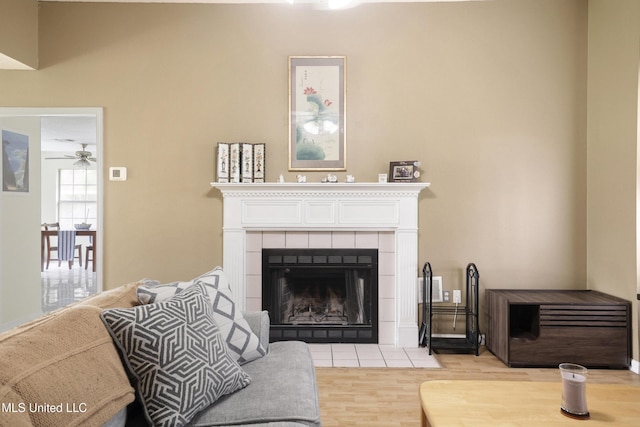 living area with light wood-type flooring, a tile fireplace, and a ceiling fan