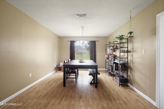 dining space with a chandelier, light wood finished floors, a textured ceiling, and baseboards