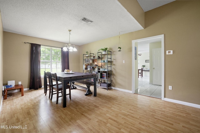 dining space featuring light wood-style flooring, a chandelier, a textured ceiling, and baseboards
