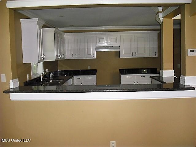 1105 Military Rd, Columbus, MS 39701 - kitchen with under cabinet range hood, a peninsula, white cabinets, dark countertops, and crown molding