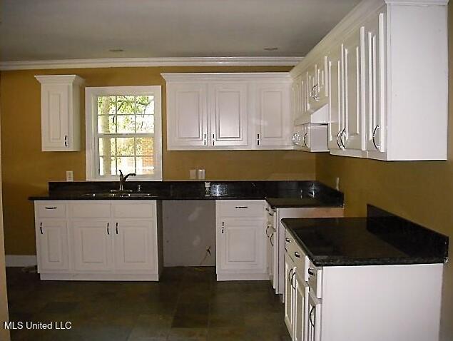 1105 Military Rd, Columbus, MS 39701 - kitchen with stove, white cabinets, under cabinet range hood, dark countertops, and ornamental molding