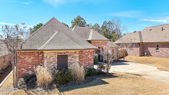 view of side of home with roof with shingles, a patio, and brick siding