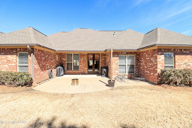 rear view of property featuring brick siding, a patio area, and roof with shingles