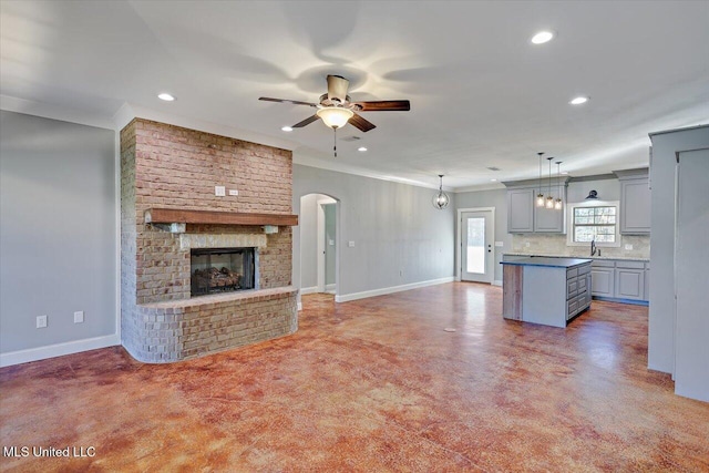 unfurnished living room featuring ceiling fan, sink, crown molding, and a brick fireplace