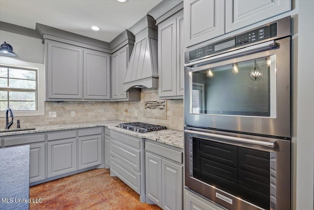 kitchen featuring light stone countertops, tasteful backsplash, custom range hood, stainless steel appliances, and sink