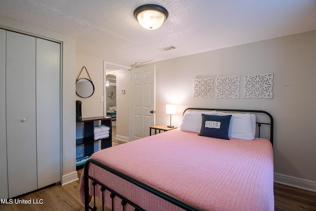 bedroom featuring a closet, wood finished floors, visible vents, and a textured ceiling