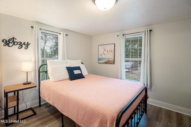 bedroom featuring multiple windows, a textured ceiling, baseboards, and dark wood-style flooring