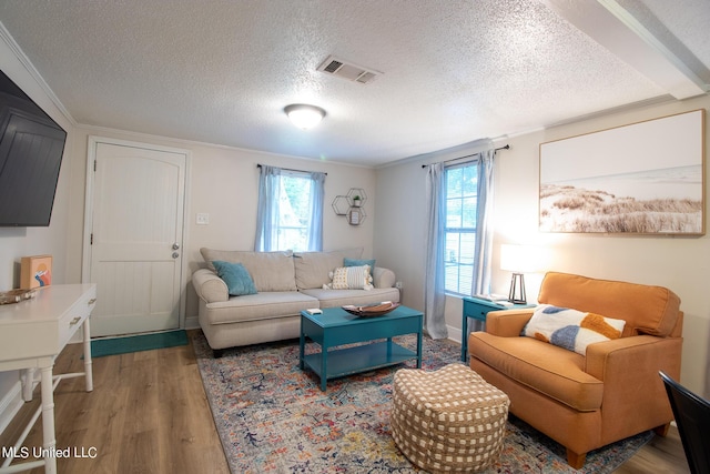 living room with a textured ceiling, wood finished floors, visible vents, and a healthy amount of sunlight
