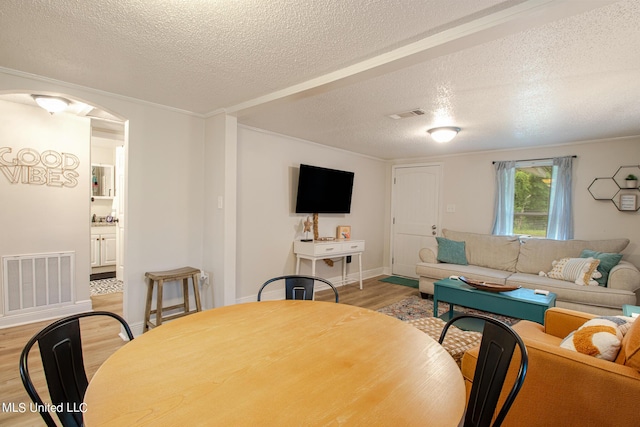 living room with a textured ceiling, light wood-type flooring, visible vents, and baseboards