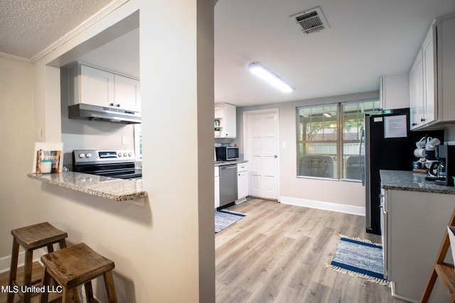 kitchen featuring light stone countertops, appliances with stainless steel finishes, white cabinetry, ornamental molding, and light hardwood / wood-style flooring