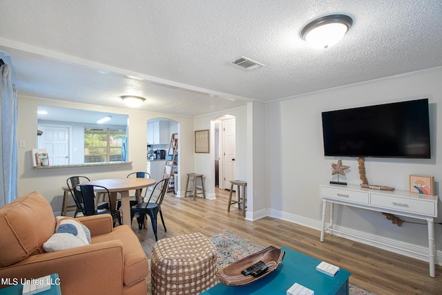 living area featuring arched walkways, a textured ceiling, baseboards, visible vents, and wood finished floors