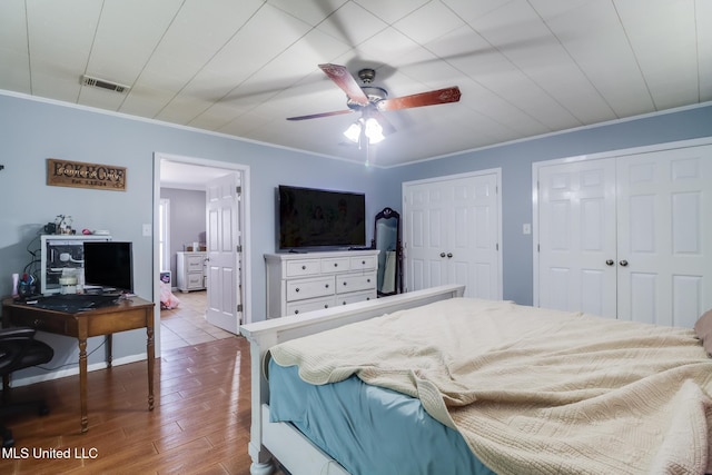 bedroom featuring multiple closets, visible vents, ornamental molding, ceiling fan, and wood finished floors