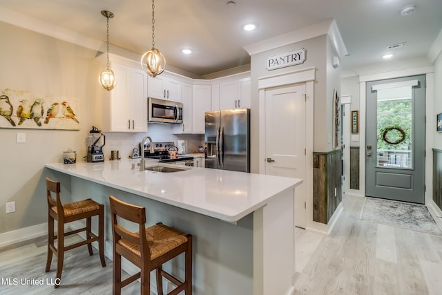 kitchen with a kitchen bar, kitchen peninsula, hanging light fixtures, white cabinetry, and stainless steel appliances