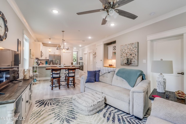 living room with a healthy amount of sunlight, crown molding, ceiling fan with notable chandelier, and light hardwood / wood-style floors