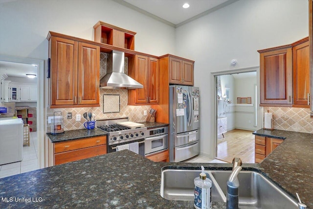 kitchen featuring stainless steel appliances, sink, washer / clothes dryer, light hardwood / wood-style flooring, and wall chimney range hood