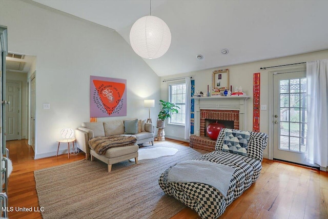 living room featuring a wealth of natural light, wood-type flooring, lofted ceiling, and a brick fireplace