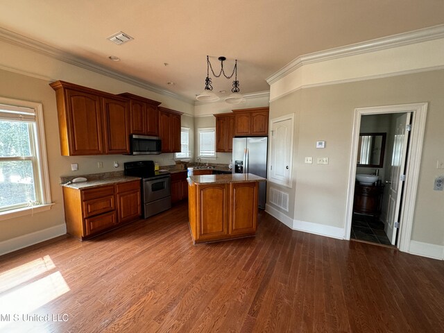 kitchen with appliances with stainless steel finishes, a center island, dark wood-type flooring, crown molding, and decorative light fixtures