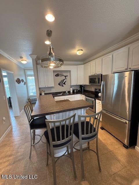 kitchen with ornamental molding, appliances with stainless steel finishes, dark countertops, and white cabinetry