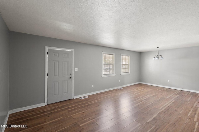 empty room with a textured ceiling, a chandelier, and dark wood-type flooring