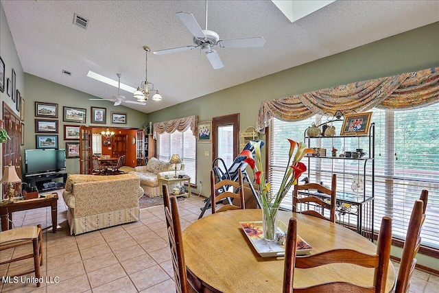 dining area featuring lofted ceiling with skylight, a textured ceiling, light tile patterned floors, and ceiling fan