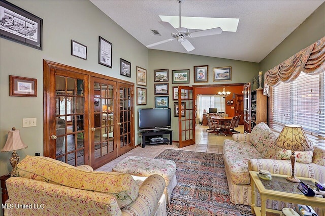 living room featuring vaulted ceiling with skylight, light tile patterned flooring, ceiling fan with notable chandelier, and a wealth of natural light