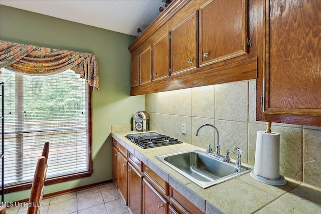 kitchen featuring decorative backsplash, light tile patterned floors, a textured ceiling, stainless steel gas cooktop, and sink