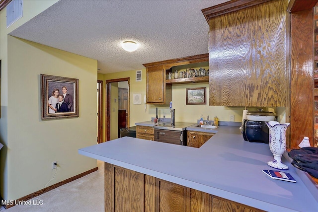 kitchen featuring a textured ceiling, sink, kitchen peninsula, and light colored carpet