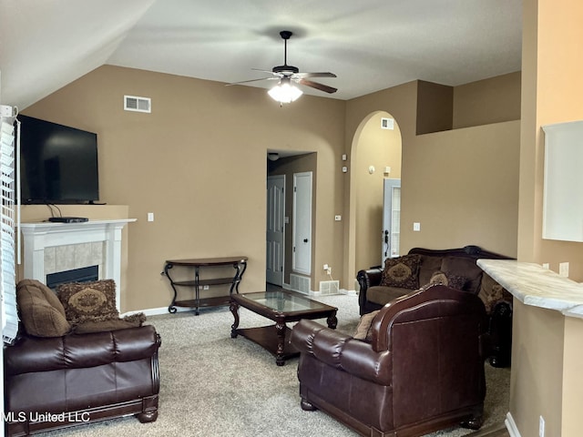 carpeted living room with a tiled fireplace, vaulted ceiling, and ceiling fan