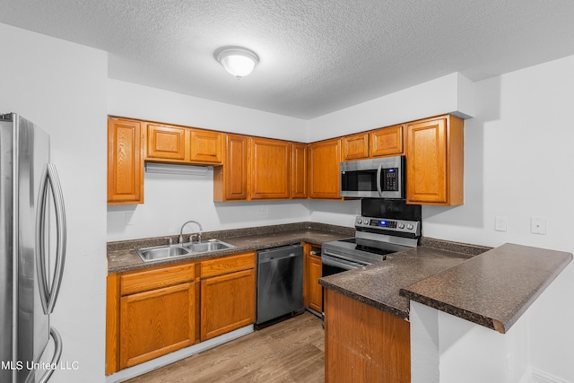 kitchen featuring kitchen peninsula, stainless steel appliances, sink, light wood-type flooring, and a textured ceiling