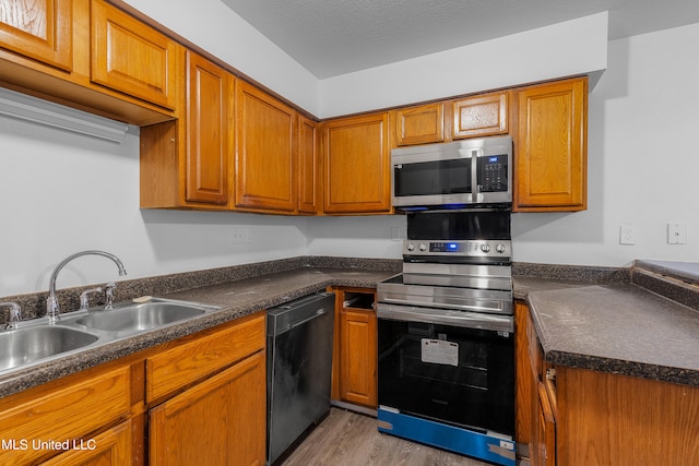 kitchen featuring sink, a textured ceiling, appliances with stainless steel finishes, and light hardwood / wood-style flooring