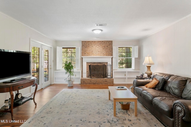 living room featuring crown molding, a brick fireplace, light wood-type flooring, and french doors