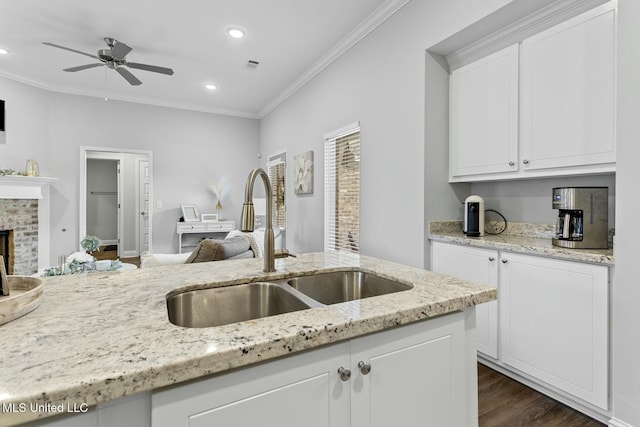 kitchen with white cabinetry, ornamental molding, open floor plan, and a sink