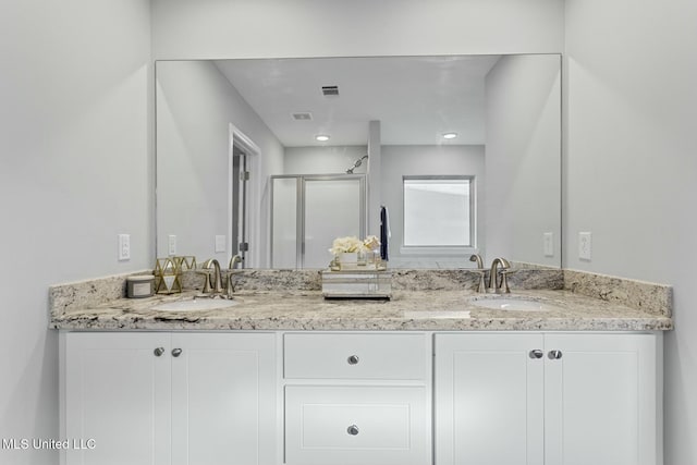 bathroom featuring a shower stall, double vanity, visible vents, and a sink