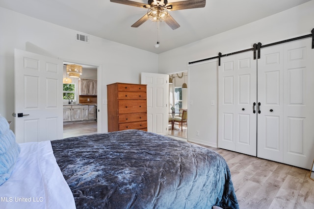 bedroom featuring sink, light wood-type flooring, a barn door, ceiling fan, and connected bathroom