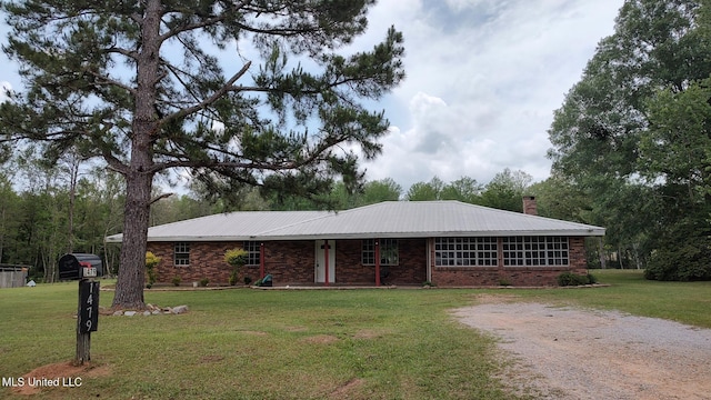 ranch-style home with a chimney, a front yard, brick siding, and metal roof