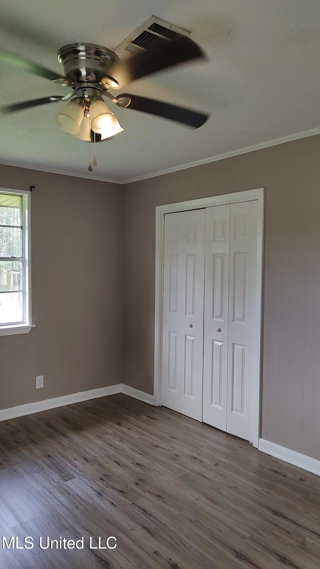 unfurnished bedroom featuring crown molding, wood finished floors, baseboards, a closet, and ceiling fan