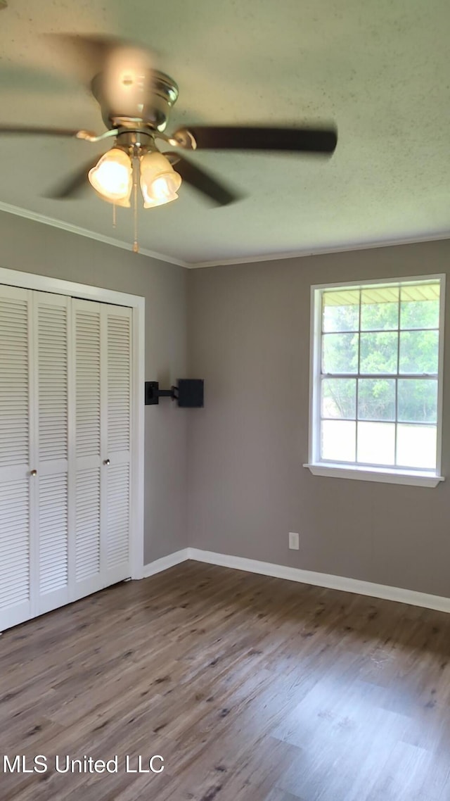 unfurnished bedroom with wood finished floors, ornamental molding, a closet, baseboards, and a ceiling fan