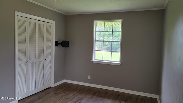 unfurnished bedroom with a closet, multiple windows, dark wood finished floors, crown molding, and baseboards