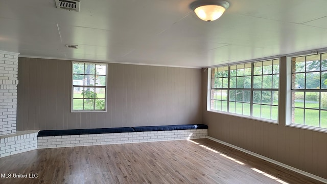 empty room with wood finished floors, healthy amount of natural light, baseboards, wood walls, and ornamental molding