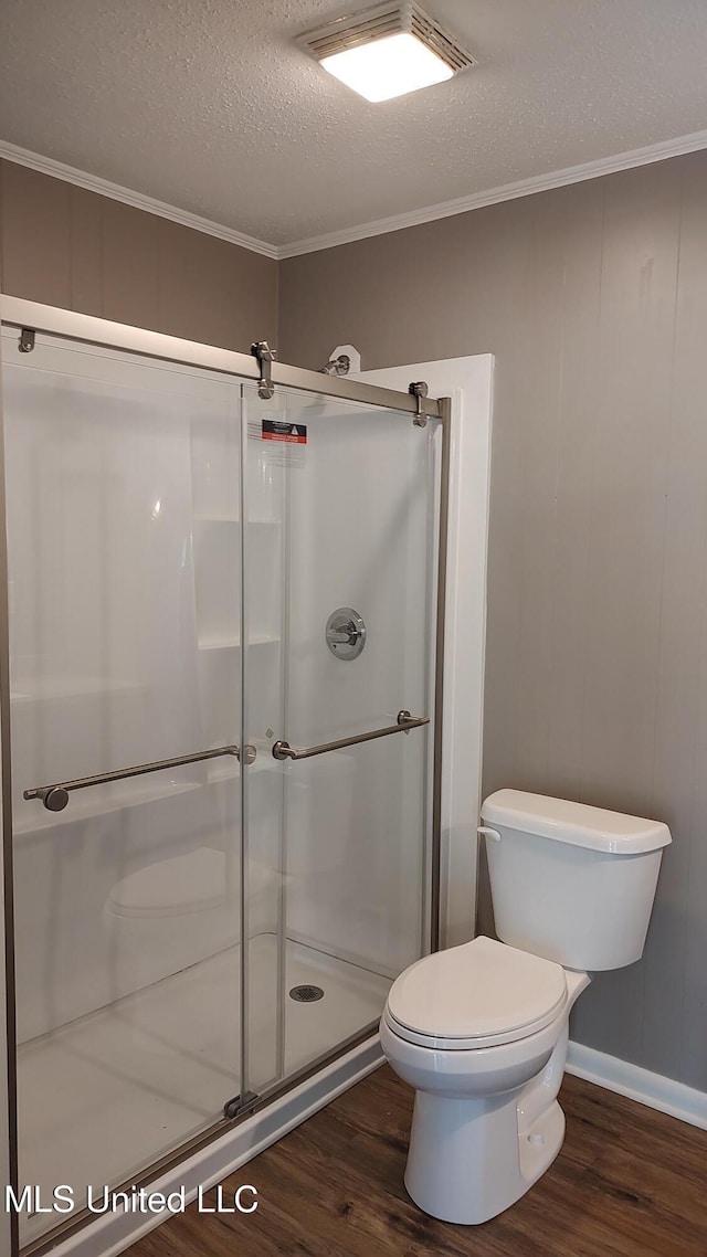 full bath with wood finished floors, a shower stall, a textured ceiling, ornamental molding, and toilet