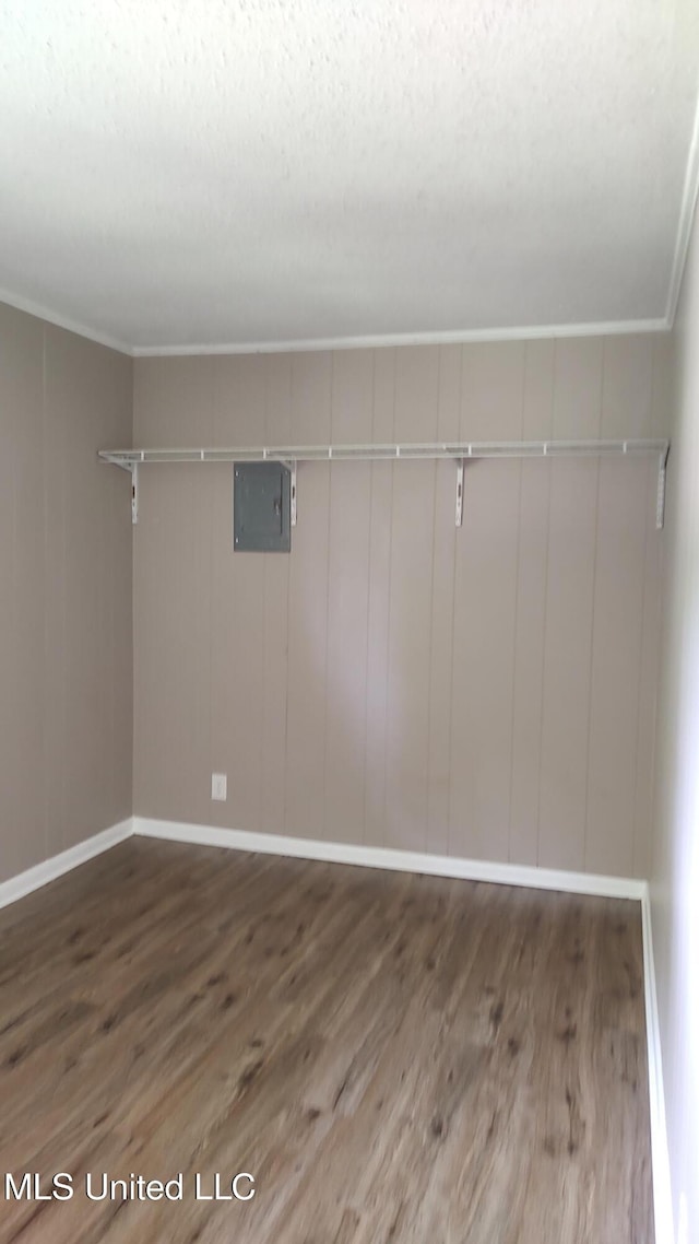 below grade area featuring wood finished floors, electric panel, ornamental molding, baseboards, and a textured ceiling