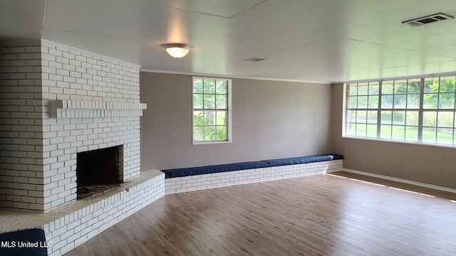 unfurnished living room featuring wood finished floors, a fireplace, healthy amount of natural light, crown molding, and wooden walls