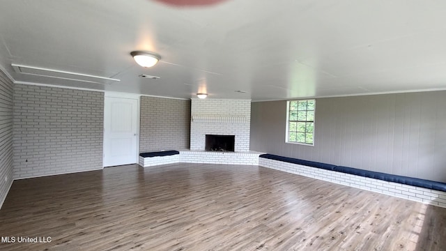 unfurnished living room with brick wall, wood finished floors, and a brick fireplace