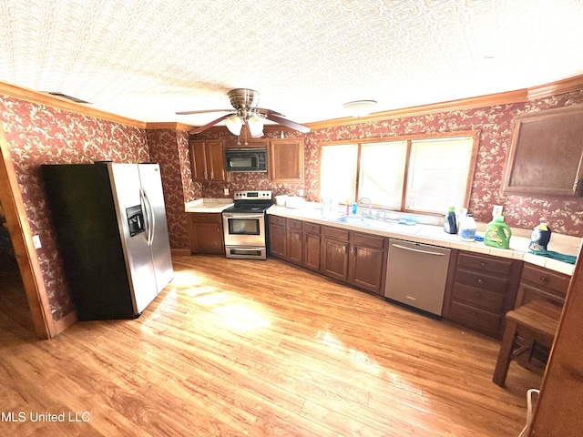 kitchen featuring dark brown cabinetry, crown molding, light hardwood / wood-style flooring, ceiling fan, and stainless steel appliances