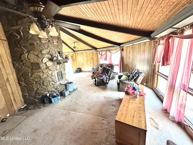 interior space featuring ceiling fan, wooden walls, a stone fireplace, and vaulted ceiling with beams