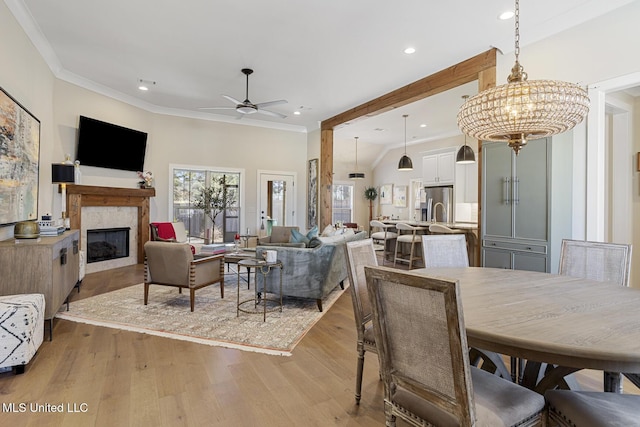 dining area featuring light wood finished floors, ceiling fan with notable chandelier, a fireplace, and ornamental molding