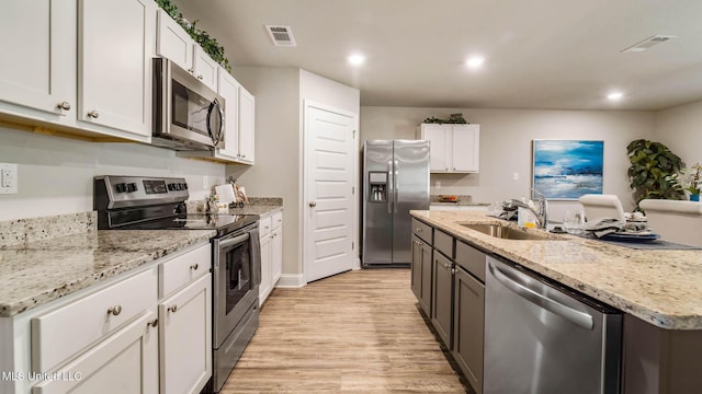 9624 Reserve Blvd, Biloxi, MS 39532 - kitchen featuring appliances with stainless steel finishes, a sink, light wood-style flooring, a kitchen island with sink, and white cabinets